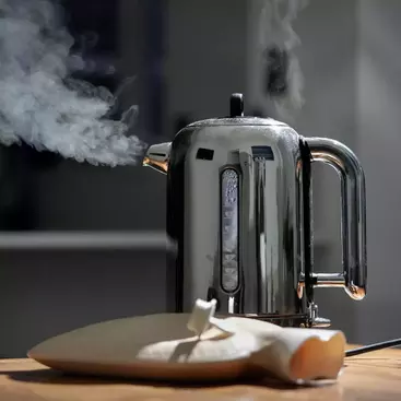 A silver kettle is boiling with streaks of steam coming out of its nozzle.