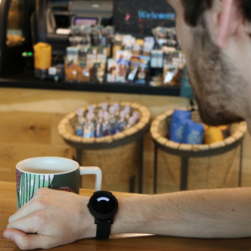 A person sitting in a coffee shop looking at the smartwatch which shows the direction of a sound occurring in the vicinity