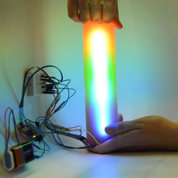 A person compressing a cylindrical object with embedded multicolor LEDs that visualize the distribution of compression force along the cylinder.