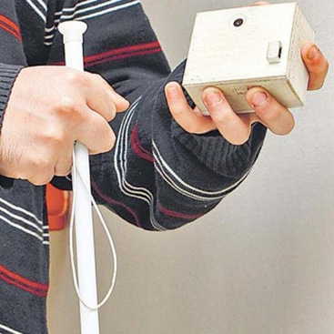 A person holding a cane in one hand and a white colored boxed device in the other hand